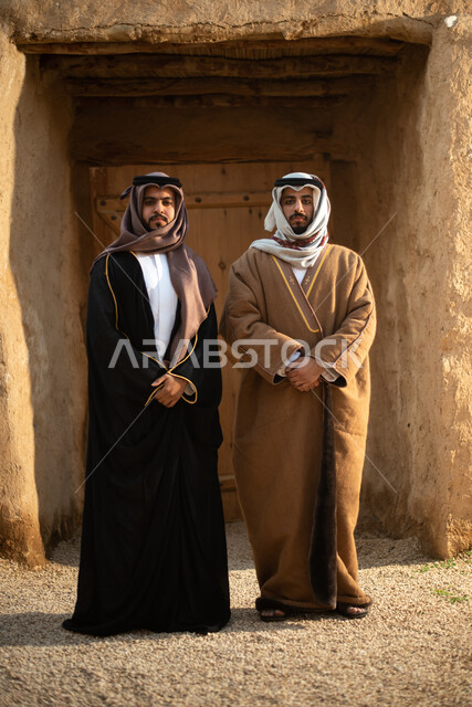 رجلان عربيان خليجيان سعوديان، يوم التأسيس السعودي، تأسيس المملكة 1727م ، أزياء شعبية سعودية، السعودية القديمة، بيوت طينية تراثية قديمة، زي تراثي سعودي للمناسبات الوطنية، صورة بالطول الكامل