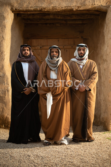مجموعة من الرجال العرب السعوديون، يوم التأسيس السعودي، تأسيس المملكة 1727م ، أزياء شعبية سعودية، السعودية القديمة، بيوت طينية تراثية قديمة، زي تراثي سعودي للمناسبات الوطنية، صورة بالطول الكامل