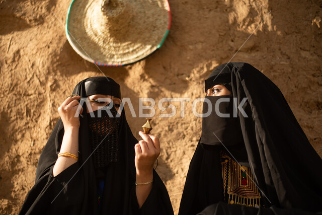 مرأتان عربيتان خليجيتان سعوديتان، إرتداء البرقع والعباءة الخليجية، الكحل العربي، يوم التأسيس السعودي، تأسيس المملكة 1727م ، أزياء شعبية سعودية، بيوت طينية تراثية قديمة