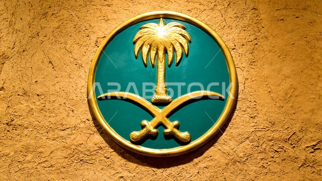 شعار المملكة العربية السعودية على حائط أثري،رمز  المملكة ، شارة دائرية ذهبية، نخلة و سيفان متقاطعان ذهبيان بخلفية خضراء، خلفية بنية خشنة