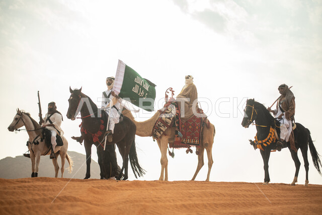 فارسان عربيان خلجيان سعوديان يمتطيان الخيول في الصحراء السعودية، استخدام البندقية السعودية، رفع العلم السعودي، ارتداء ازياء شعبية تراثية، رجل ملثم يركب الجمل، احياء ذكرى التاسيس السعودي، الدولة السعودية الاولى 1727م، يوم التاسيس السعودي، عيد وطني سعودي
