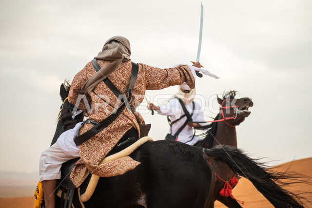 فارسان عربيان خليجيان سعوديان يمتطيان الخيل في الصحراء السعودية ويتبارزان، مبارزة السيوف، ارتداء زي تراثي شعبي، احياء ذكرى التاسيس السعودي، الدولة السعودية الاولى 1727م، يوم التاسيس السعودي، عيد وطني سعودي