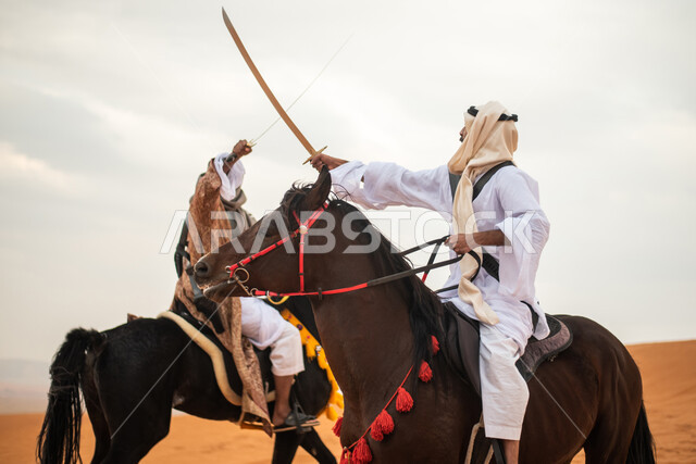فارسان عربيان خليجيان سعوديان يمتطيان الخيل في الصحراء السعودية ويتبارزان، مبارزة السيوف، ارتداء زي تراثي شعبي، احياء ذكرى التاسيس السعودي، الدولة السعودية الاولى 1727م، يوم التاسيس السعودي، عيد وطني سعودي