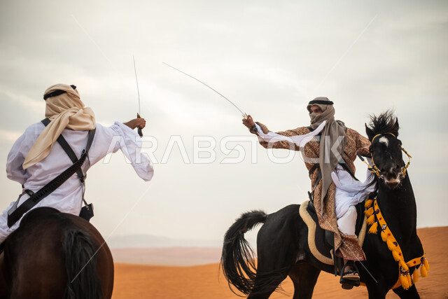 فارسان عربيان خليجيان سعوديان يمتطيان الخيل في الصحراء السعودية ويتبارزان، مبارزة السيوف، ارتداء زي تراثي شعبي، احياء ذكرى التاسيس السعودي، الدولة السعودية الاولى 1727م، يوم التاسيس السعودي، عيد وطني سعودي