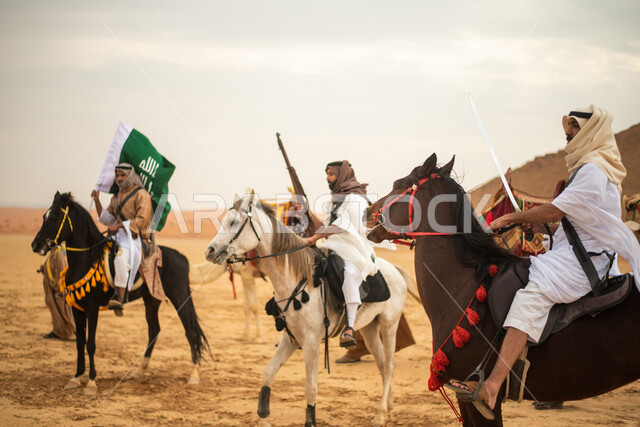 فرسان عرب خلجيين سعوديين يمتطون الخيول في الصحراء السعودية، استخدام السيوف والبنادق، رفع العلم السعودي، ارتداء ازياء شعبية تراثية، احياء ذكرى التاسيس السعودي، الدولة السعودية الاولى 1727م، يوم التاسيس السعودي، عيد وطني سعودي