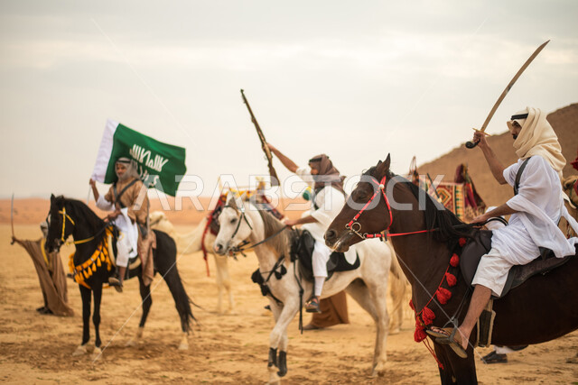 فرسان عرب خلجيين سعوديين يمتطون الخيول في الصحراء السعودية، استخدام السيوف والبنادق، رفع العلم السعودي، ارتداء ازياء شعبية تراثية، احياء ذكرى التاسيس السعودي، الدولة السعودية الاولى 1727م، يوم التاسيس السعودي، عيد وطني سعودي