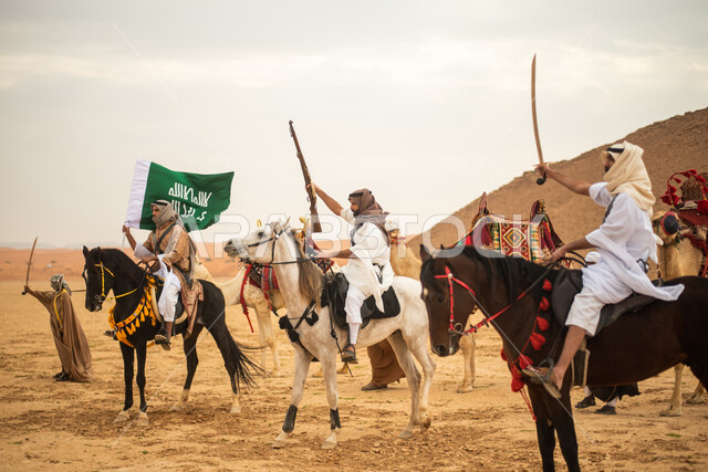 فرسان عرب خلجيين سعوديين يمتطون الخيول في الصحراء السعودية، استخدام السيوف والبنادق، رفع العلم السعودي، ارتداء ازياء شعبية تراثية، احياء ذكرى التاسيس السعودي، الدولة السعودية الاولى 1727م، يوم التاسيس السعودي، عيد وطني سعودي
