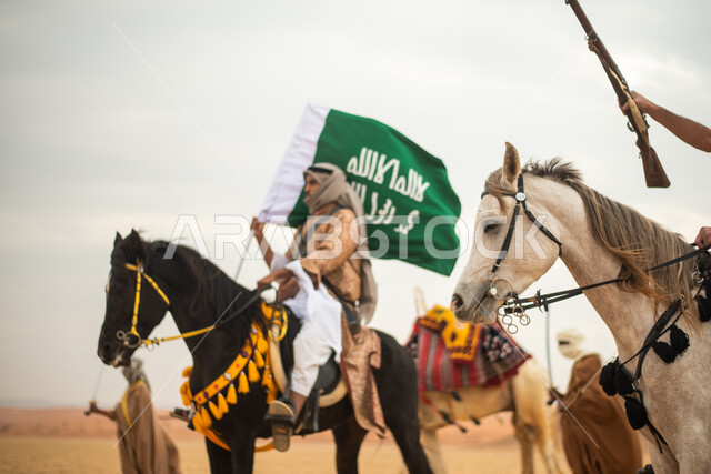 Saudi Gulf Arab knights riding horses in the Saudi desert, using the Saudi rifle, raising the Saudi flag, wearing traditional folk costumes, commemorating the Saudi founding, the first Saudi state 1727 AD, Saudi founding day, Saudi national holiday