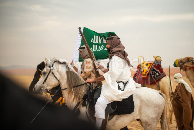 فرسان عرب خلجيين سعوديين يمتطون الخيول في الصحراء السعودية، استخدام السيوف والبنادق، رفع العلم السعودي، ارتداء ازياء شعبية تراثية، احياء ذكرى التاسيس السعودي، الدولة السعودية الاولى 1727م، يوم التاسيس السعودي، عيد وطني سعودي