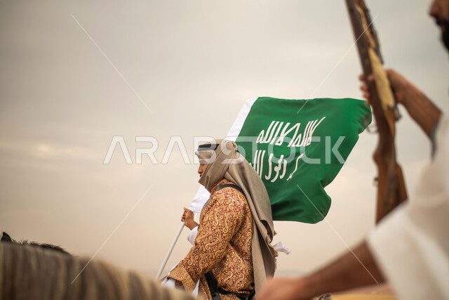 Saudi Gulf Arab knights riding horses in the Saudi desert, using the Saudi rifle, raising the Saudi flag, wearing traditional folk costumes, commemorating the Saudi founding, the first Saudi state 1727 AD, Saudi founding day, Saudi national holiday