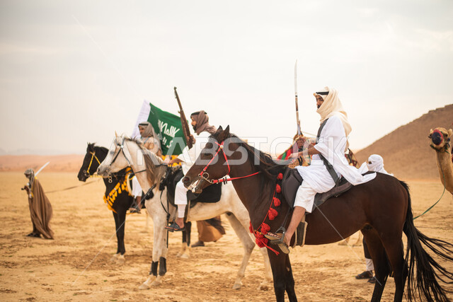 فرسان عرب خلجيين سعوديين يمتطون الخيول في الصحراء السعودية، استخدام السيوف والبنادق، رفع العلم السعودي، ارتداء ازياء شعبية تراثية، احياء ذكرى التاسيس السعودي، الدولة السعودية الاولى 1727م، يوم التاسيس السعودي، عيد وطني سعودي