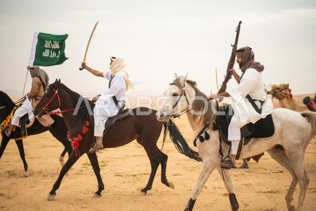فرسان عرب خلجيين سعوديين يمتطون الخيول في الصحراء السعودية، استخدام السيوف والبنادق، رفع العلم السعودي، ارتداء ازياء شعبية تراثية، احياء ذكرى التاسيس السعودي، الدولة السعودية الاولى 1727م، يوم التاسيس السعودي، عيد وطني سعودي