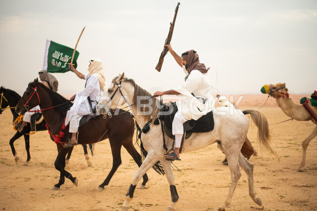 فرسان عرب خلجيين سعوديين يمتطون الخيول في الصحراء السعودية، استخدام السيوف والبنادق، رفع العلم السعودي، ارتداء ازياء شعبية تراثية، احياء ذكرى التاسيس السعودي، الدولة السعودية الاولى 1727م، يوم التاسيس السعودي، عيد وطني سعودي