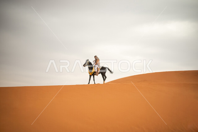 فارس عربي خلجي سعودي يمتطي الخيل في الصحراء السعودية، استخدام السيف السعودي، ارتداء ازياء شعبية تراثية، احياء ذكرى التاسيس السعودي، الدولة السعودية الاولى 1727م، يوم التاسيس السعودي، عيد وطني سعودي