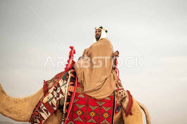 رجل عربي خليجي سعودي يمتطي الجمل في الصحراء السعودية، ارتداء ازياء شعبية تراثية، احياء ذكرى التاسيس السعودي، الدولة السعودية الاولى 1727م، يوم التاسيس السعودي، عيد وطني سعودي