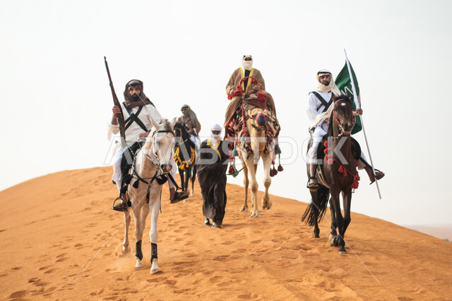 فرسان عرب خلجيين سعوديين يمتطون الخيول في الصحراء السعودية، استخدام السيوف والبنادق، رفع العلم السعودي، ارتداء ازياء شعبية تراثية، احياء ذكرى التاسيس السعودي، الدولة السعودية الاولى 1727م، يوم التاسيس السعودي، عيد وطني سعودي