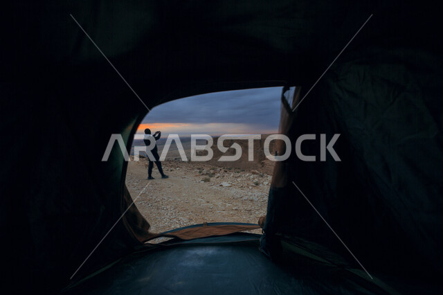 صورة من داخل خيمة لشاب يلتقط الصور في الصحراء وقت غروب الشمس، الطبيعية الخلابة، رحلة بر، التخييم في البر، الطبيعة الصحراوية