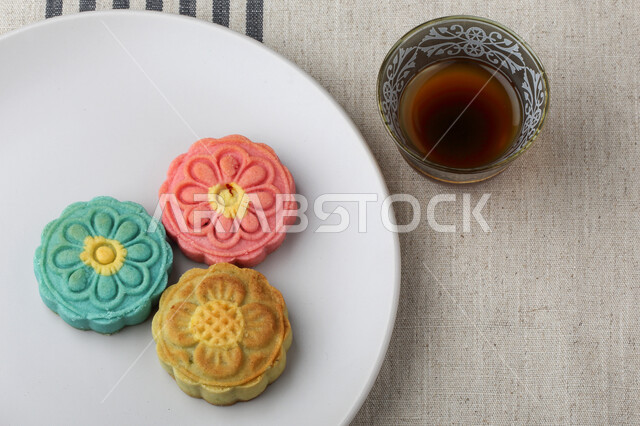 معمول التمر ملون مربع الشكل ، الحلويات الشعبية الهشة على لوح خشبي ، كعك العيد , قهوة عربية ، الضيافة و الاستقبال