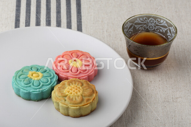 معمول التمر ملون مربع الشكل ، الحلويات الشعبية الهشة على لوح خشبي ، كعك العيد , قهوة عربية ، الضيافة و الاستقبال