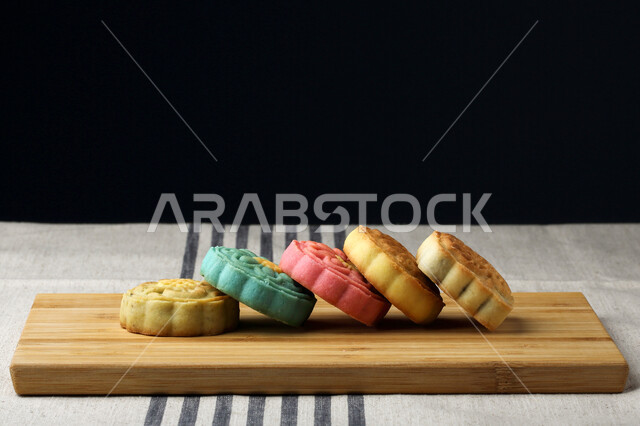 معمول التمر ملون مربع الشكل ، الحلويات الشعبية الهشة على لوح خشبي ، كعك العيد , خلفية سوداء