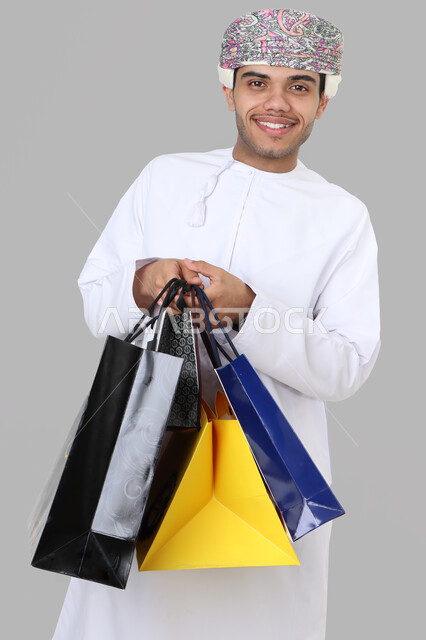 بورتريه لرجل عربي عماني خليجي يرتدي اللباس التقليدي , يحمل مشترياته من المركز التجاري , العوده من السوق , متعة التسوق , شراء الأغراض الضروريه , أكياس ورقية .