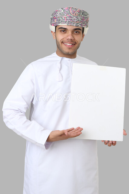 بورتريه لرجل عربي عماني خليجي باللباس التقليدي , يقوم بإيماءات وجه مختلفة ، يحمل بيده لوح أبيض , لوحة إعلانية فارغة ، خلفية رمادية .