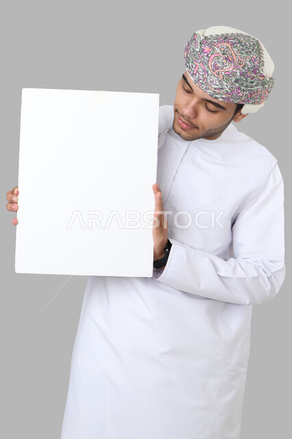 بورتريه لرجل عربي عماني خليجي باللباس التقليدي , يقوم بإيماءات وجه مختلفة ، يحمل بيده لوح أبيض , لوحة إعلانية فارغة ، خلفية رمادية .