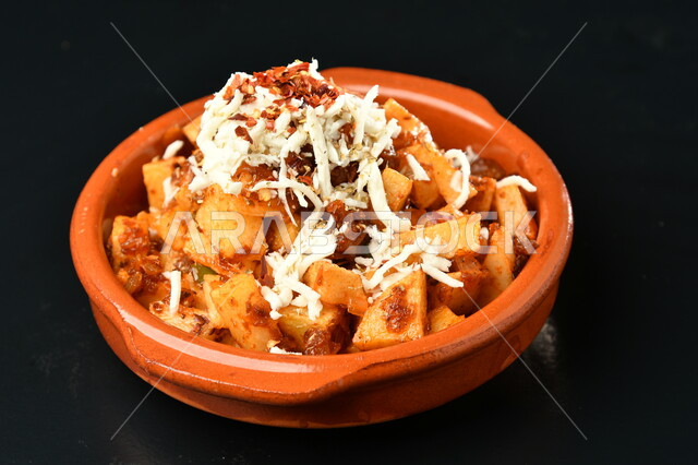 طبق بطاطس متبلة مع الجبنة على سطح أسود ، مأكولات عربية