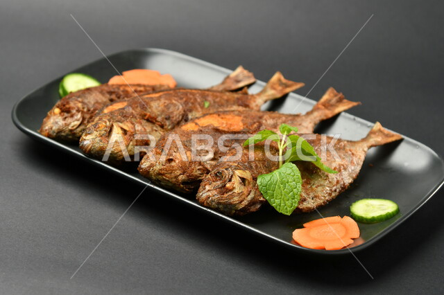 طبق من السمك المقلي المتبل على سطح أسود ، مأكولات بحرية ، مأكولات عربية ، وجبة طعام غذائية صحية ، صيادية سمك