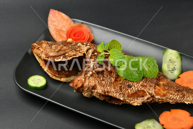 طبق من السمك المقلي المتبل على سطح أسود ، مأكولات بحرية ، مأكولات عربية ، وجبة طعام غذائية صحية ، صيادية سمك