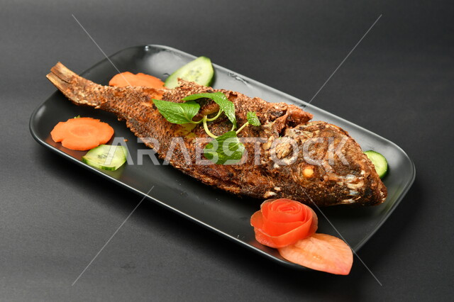 طبق من السمك المقلي المتبل على سطح أسود ، مأكولات بحرية ، مأكولات عربية ، وجبة طعام غذائية صحية ، صيادية سمك