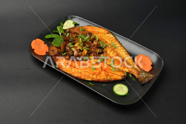 طبق من السمك المقلي المتبل على سطح أسود ، مأكولات بحرية ، مأكولات عربية ، وجبة طعام غذائية صحية ، صيادية سمك