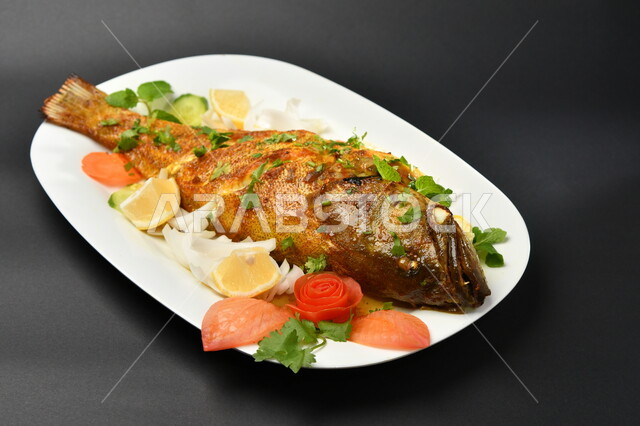 طبق من السمك المقلي المتبل على سطح أسود ، مأكولات بحرية ، مأكولات عربية ، وجبة طعام غذائية صحية ، صيادية سمك