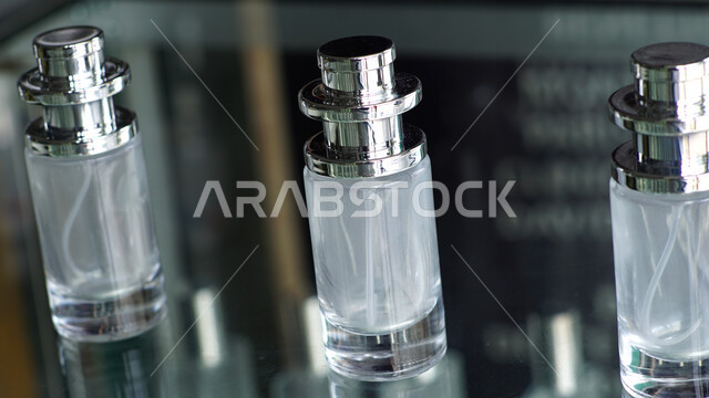 زجاجات عطور شفافة فارغة اسطوانية الشكل على طاولة زجاجية، التسويق لمنتجات العطور، التطيب والتعطر