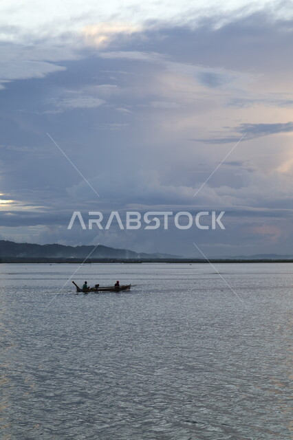 سفينة تبحر وسط البحر وقت غروب الشمس، غيوم كثيفة فوق البحر، هدوء واسترخاء، جمال طبيعة الغيوم والبحار