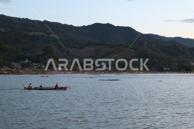 A fisherman sailing his boat during sunset with mountains full of trees behind him, the beauty of the nature of the mountains and seas