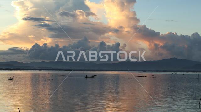 صياد يبحر بزورقه أثناء غروب الشمس، أشعة الشمس بين الغيوم، جمال طبيعة الغيوم والبحار