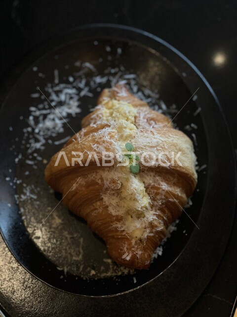 وجبة فطور كرواسون مع الجبنة المرشوشة على صحن أسود، معجنات و مخبوزات عربية ، مأكولات ووجبات افطار شهية