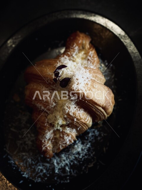 وجبة فطور كرواسون مع الجبنة المرشوشة على صحن أسود، معجنات و مخبوزات عربية ، مأكولات ووجبات افطار شهية