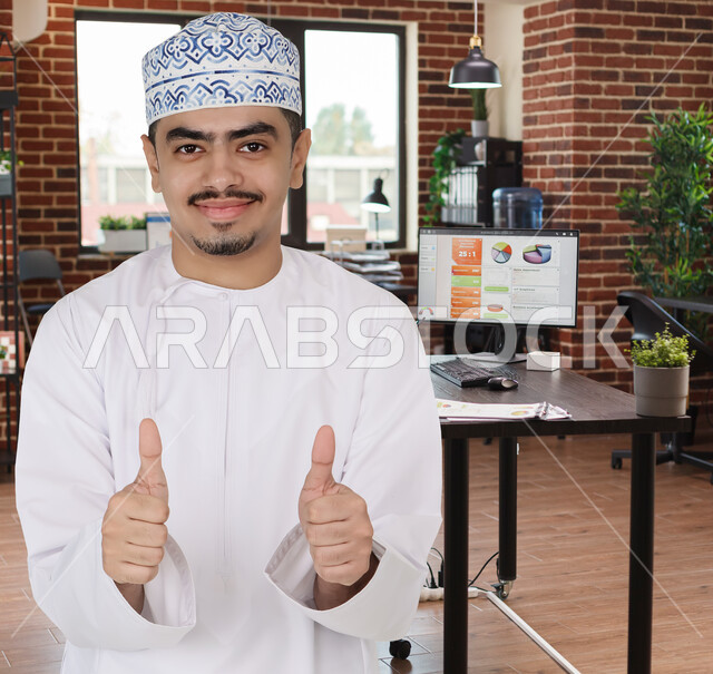 رجل عربي خليجي عماني يرفع اصبع الابهام لاعلى، ايماءات وجه مبتسمة ويدين تدل على القبول والموافقة، الاعجاب، حركة واشارات، اعمال مكتبية، مقر العمل