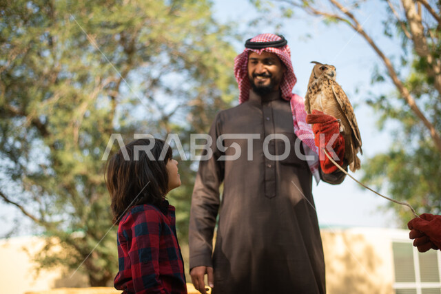 رجل عربي خليجي سعودي مع إبنه، قضاء أوقات ممتعة في حديقة الحيوانات، أماكن سياحية ترفيهية، أنشطة ترفيهية مع الطيور، تربية وتدريب الطيور الجارحة في المحمية الطبيعية، طائر البومة