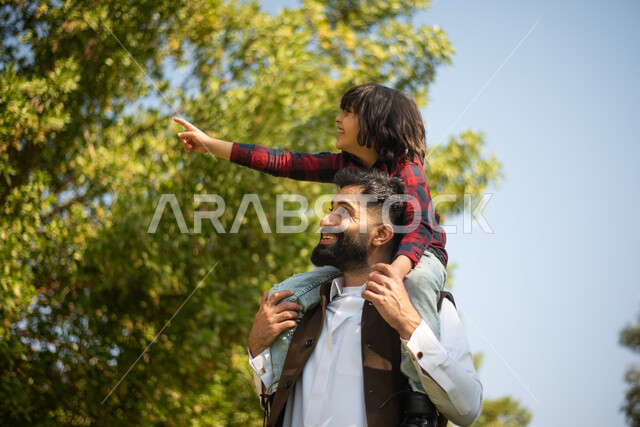 رجل عربي خليجي سعودي يقضي أوقات ممتعه مع ابنه، اللعب في إحدى الحدائق العامة في السعودية، نزهة في الهواء الطلق، جولة في الطبيعة الخضراء، أنشطة ترفيهية عائلية، عطلة صيفية