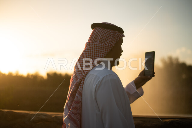 رجل عربي خليجي سعودي يقضي أوقات ممتعة في احد الحدائق العامة، استخدام الهاتف المحمول، التقاط صور تذكارية، بث مباشر، منتجع ترفيهي وقت غروب الشمس، جولة في الطبيعة الخضراء، أنشطة ترفيهية، التنزه في الهواء الطلق
