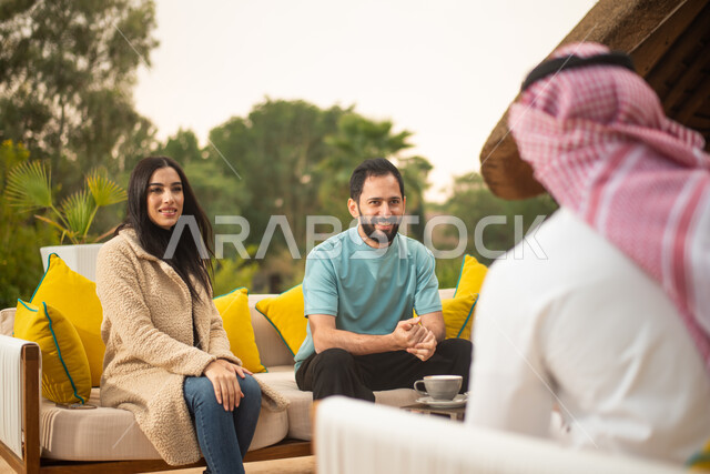 امرأة ورجلان عرب خليجيين سعوديين يتبادلون الحديث في احد المقاهي السعودية، ستمتعون بتبادل الحديث في احد الاماكن الترفيهية، نقاشات وحوارات، قضاء اوقات ممتعة، منتزهات سعودية، وناسة وتعارف، الجلوس في الهواء الطلق