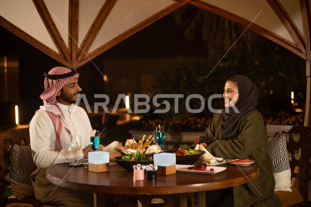 زوجان عربيان خليجيان سعوديان يستمتعان بتبادل الحديث  في احد المقاهي السعودية، نقاشات وحوارات، قضاء أوقات ممتعة، تناول المشروبات الباردة، أجواء عائلية سعيدة، مقهى سعودي