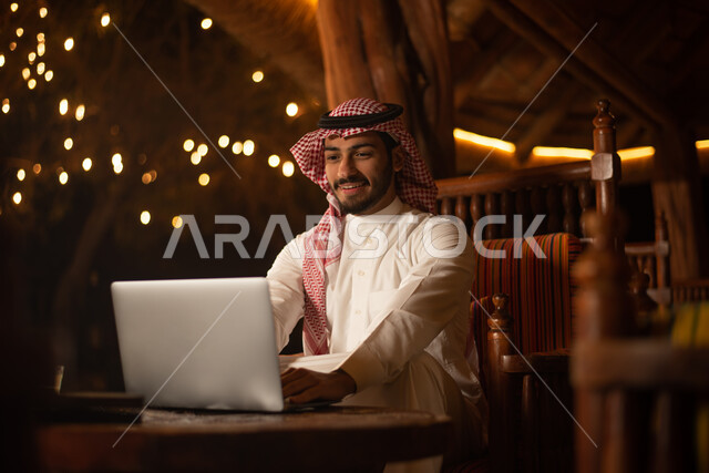 A Saudi Arabian Gulf man using a laptop, working remotely, completing work tasks, surfing the Internet, using modern technologies, gardens and parks