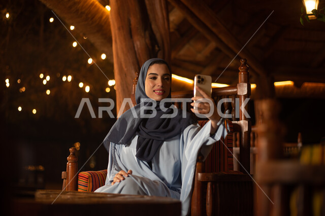 امرأة عربية خليجية سعودية تستخدم الهاتف المحمول، التقاط صور تذكارية، كاميرا امامية، صور سيلفي، بث مباشر، ايماءات وجه سعيدة، استخدام تقنيات حديثة