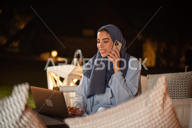 امرأة عربية خليجية سعودية تستخدم الحاسوب المحمول وتجري مكالمة هاتفية، العمل عن بعد، التواصل مع العملاء، التسويق الالكتروني، انجاز مهام العمل، استخدام تقنيات حديثة، حدائق ومنتزهات