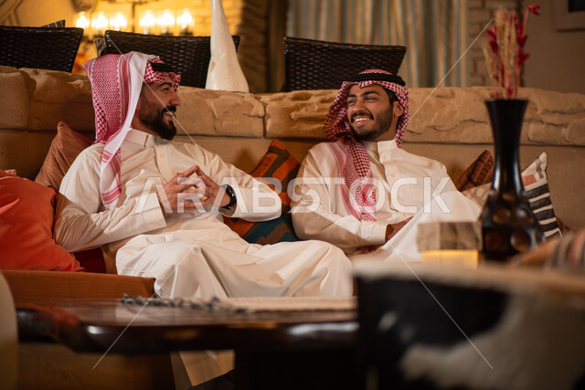 رجلان عربيان خليجيان سعوديان يرتديان الزي السعودي ويقضيان اوقات ممتعة، نقاشات وحوارات، صداقات شباب، ايماءات وجه سعيدة، جلسة شبابية