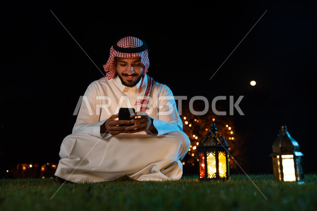 رجل عربي خليجي سعودي يستخدم الهاتف المحمول، فانوس رمضان، التواصل الاجتماعي، تصفح المواقع الالكترونية، شهر رمضان المبارك، إضاءة وزينة شهر رمضان، أجواء رمضانية، مناسبات دينية